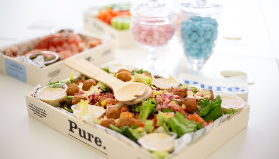 A catered lunch of salad in a delivery box with other options in the background.
