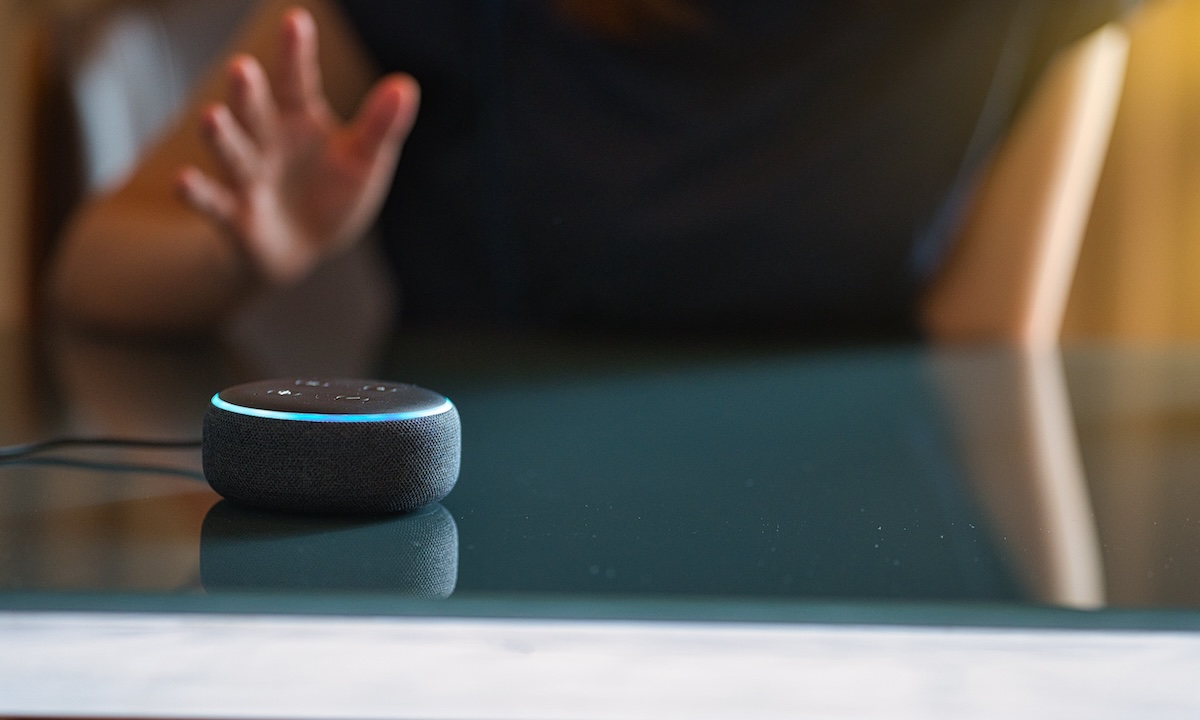 Woman sitting at desk talking to voice device in foreground