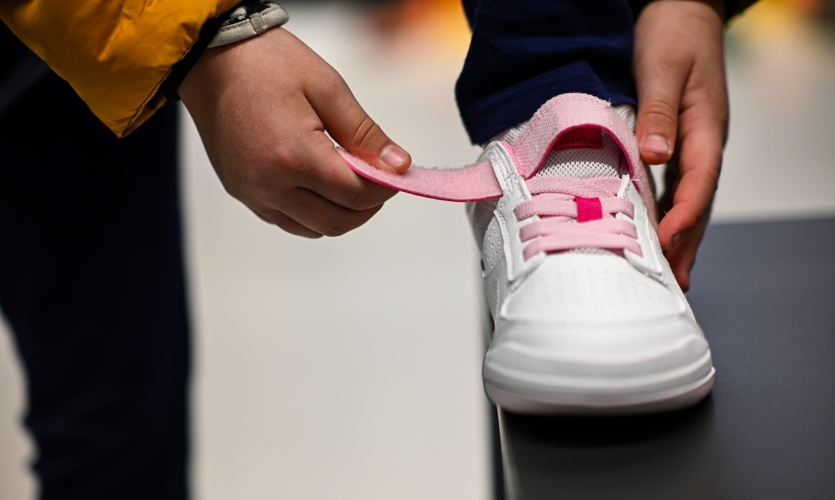 Picture of fastening a child's shoe with velcro strap and pink laces.